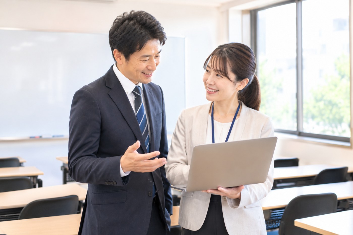 塾の教室でノートPCを手に笑顔で話す教室長と講師