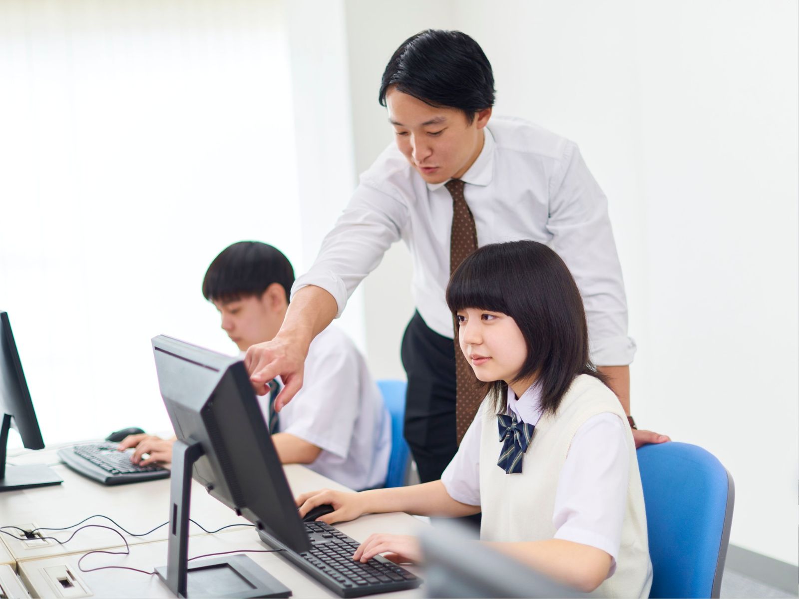 学習塾でノートパソコンを開き、教材を手に授業の準備をする女性講師