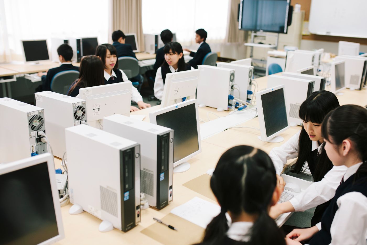 デスクトップPCが並ぶPC教室で授業を受ける生徒たちと教員